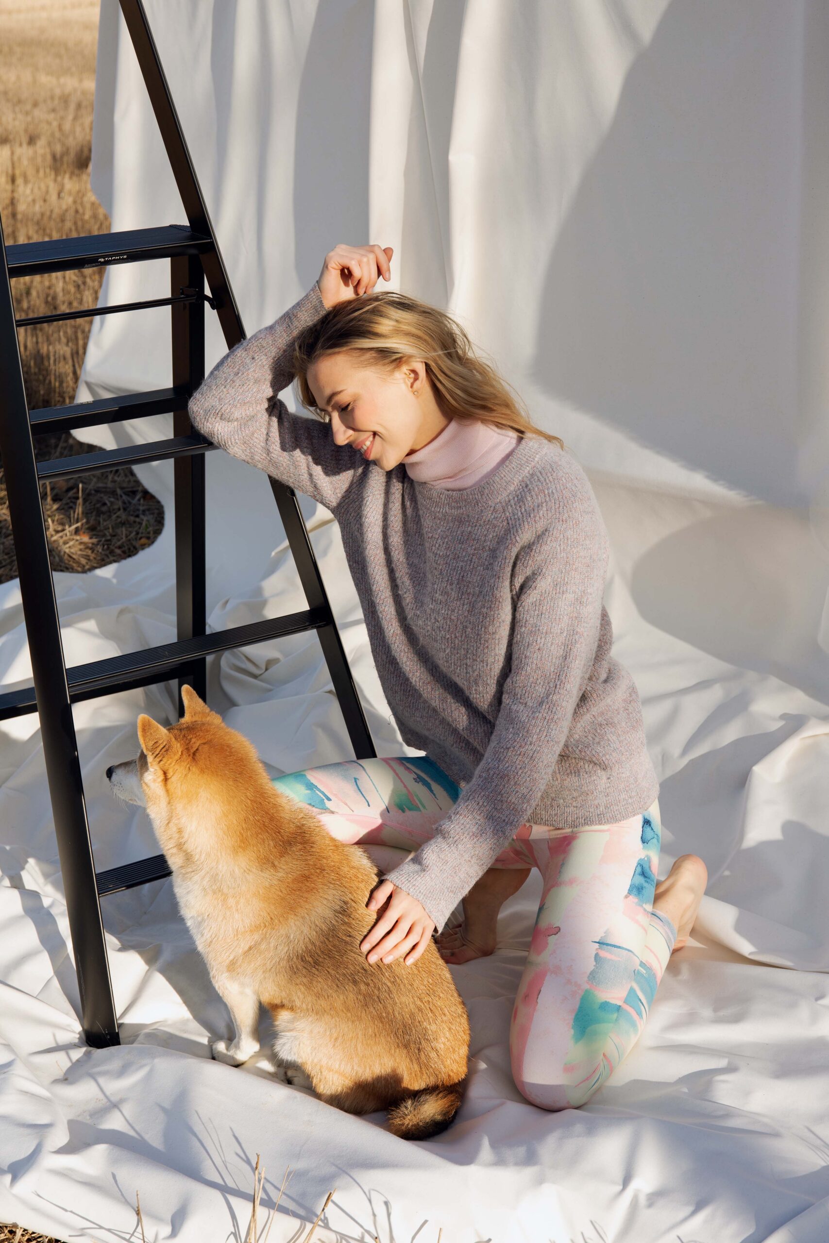 Kneeling woman petting a dog, wearing Weeping birch - Soahki Nordic Savannah pastel watercolor print leggings with a grey-lilac knit sweater