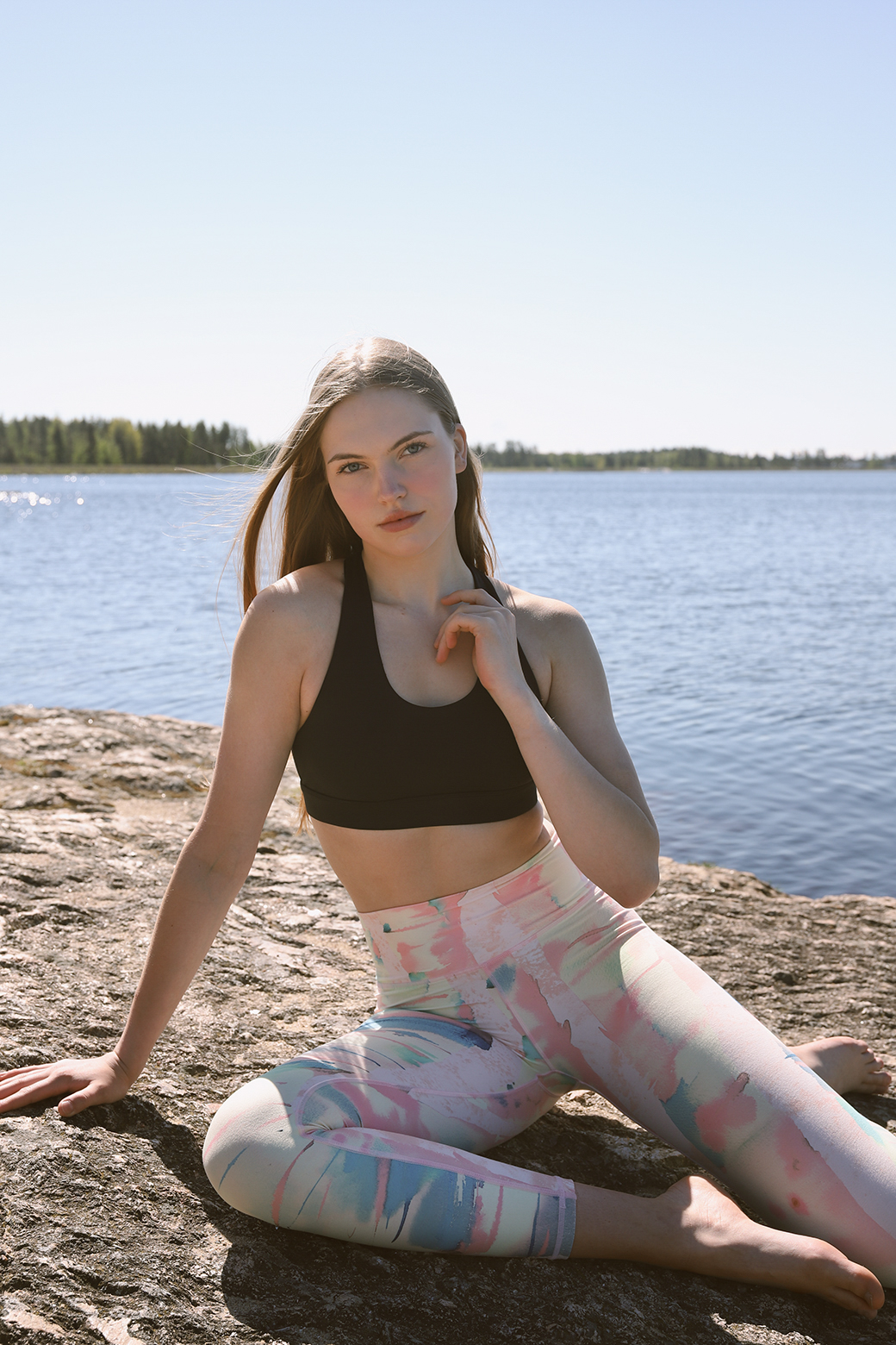 Woman sitting cross-legged on a sunlit rock by a lake wearing Weeping birch - Soahki Nordic Savannah watercolor print leggings