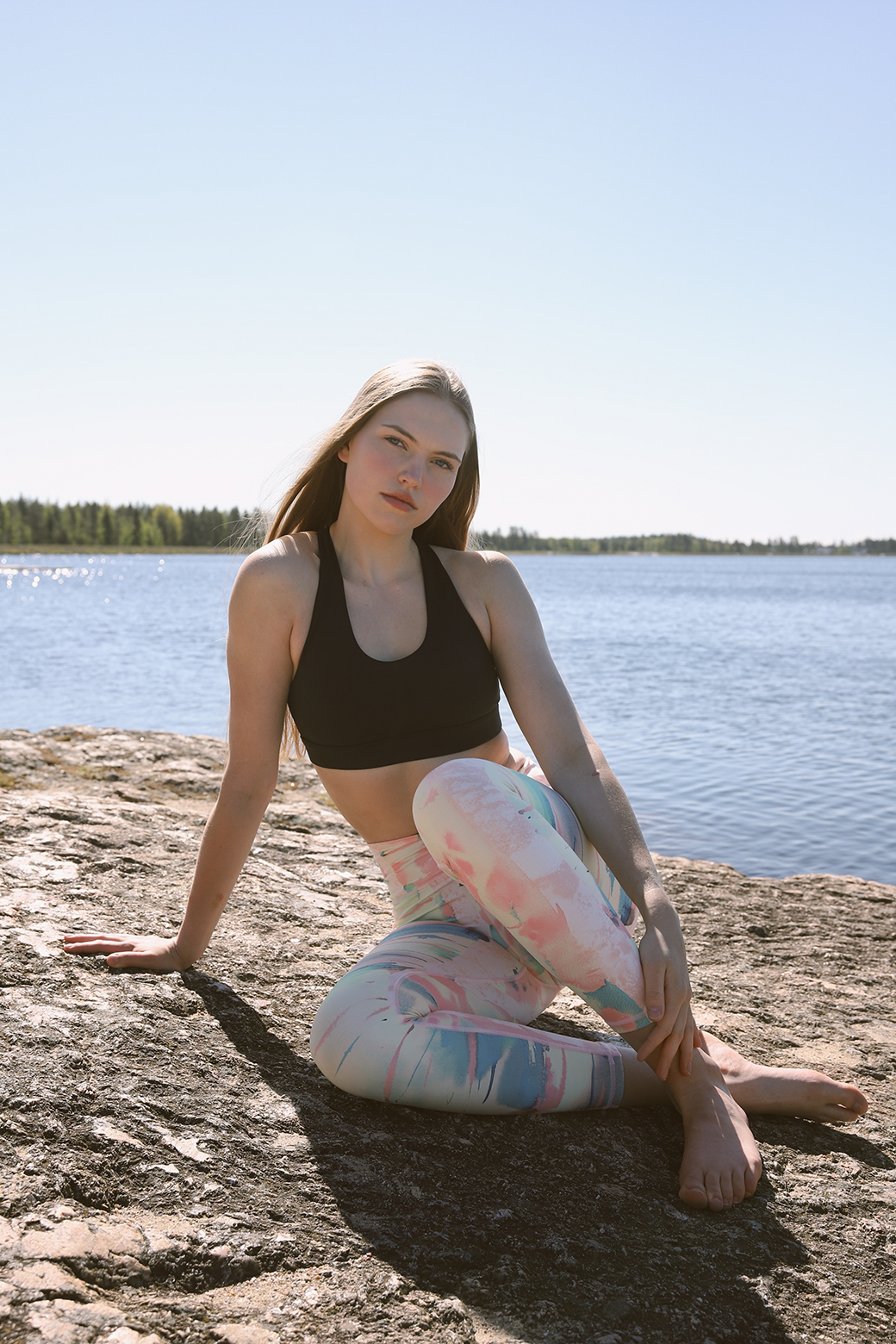 Model seated on rocky lakeshore wearing pastel Weeping birch - Soahki Nordic Savannah print sustainable yoga leggings