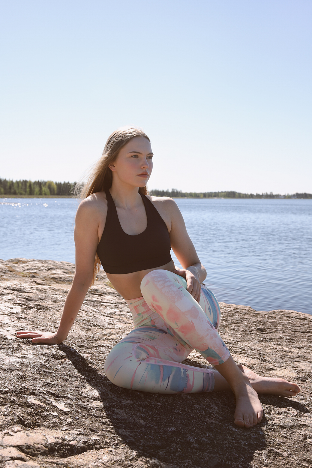 Woman seated on rocks by a lake wearing Weeping birch - Soahki Nordic Savannah pastel print yoga leggings and black sports bra