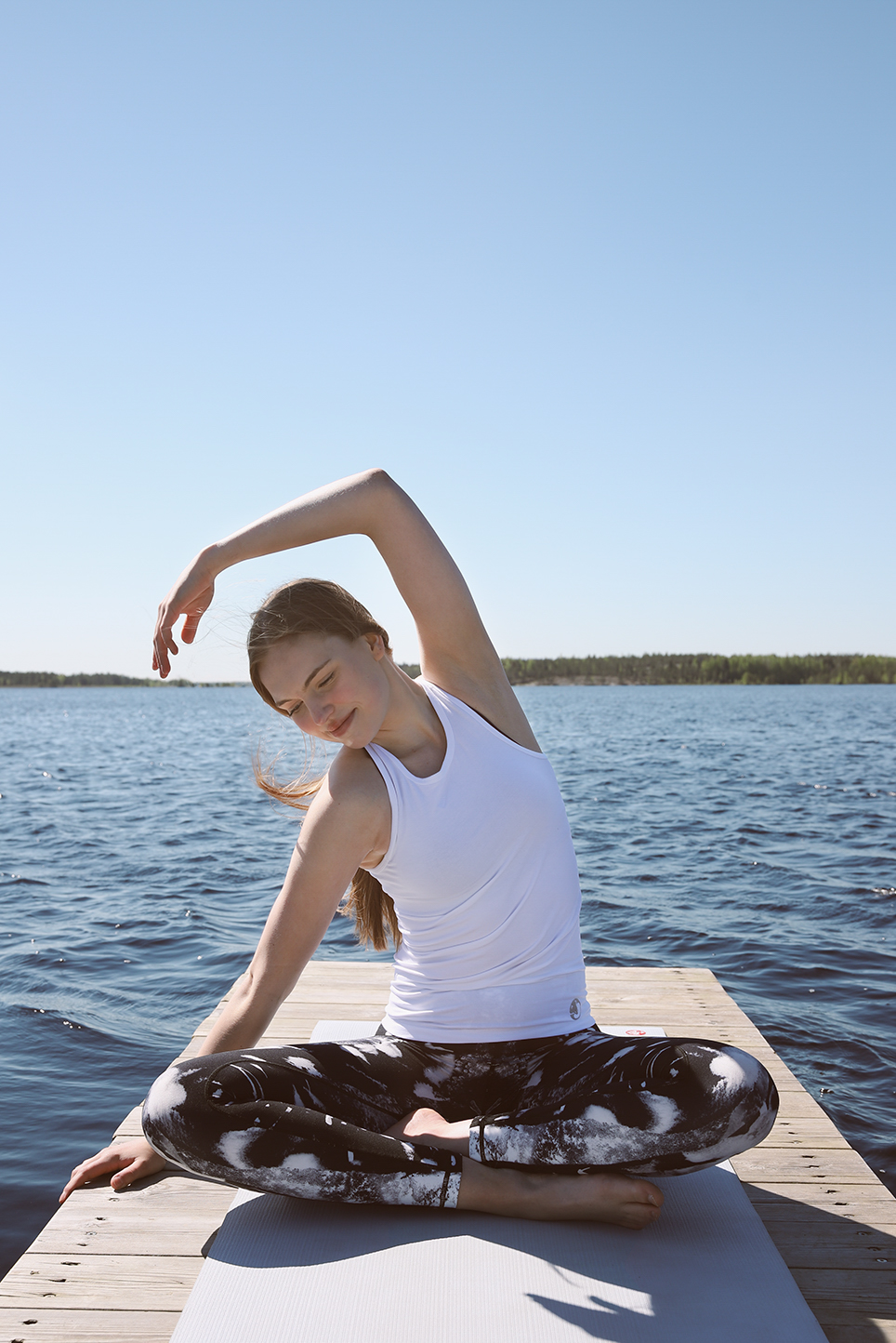 Woman stretching, wearing Organic Yang white tank top on a lakeside dock